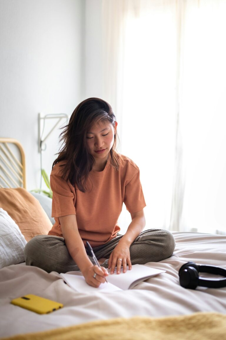 Asian female teen college student sitting on bed writing on journal in bedroom.Copy space.Vertical. An Krisen wachsen